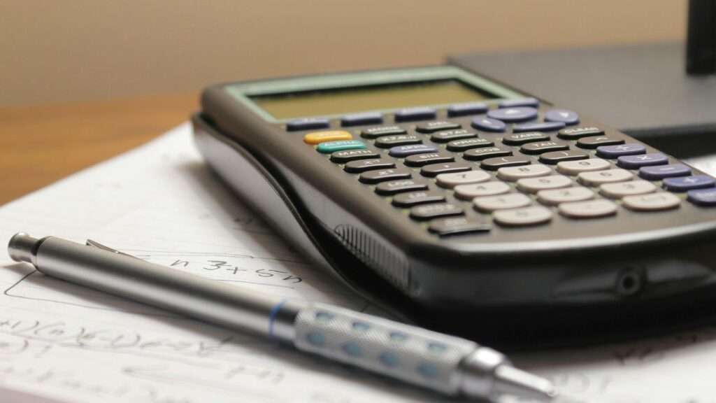 Calculadora de oficina junto a una libreta de notas con apuntes financieros sobre una mesa de madera