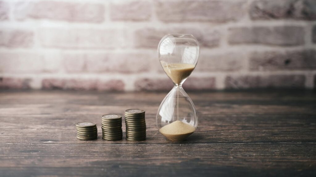 Reloj de arena con monedas representando el valor del tiempo en la inversión.